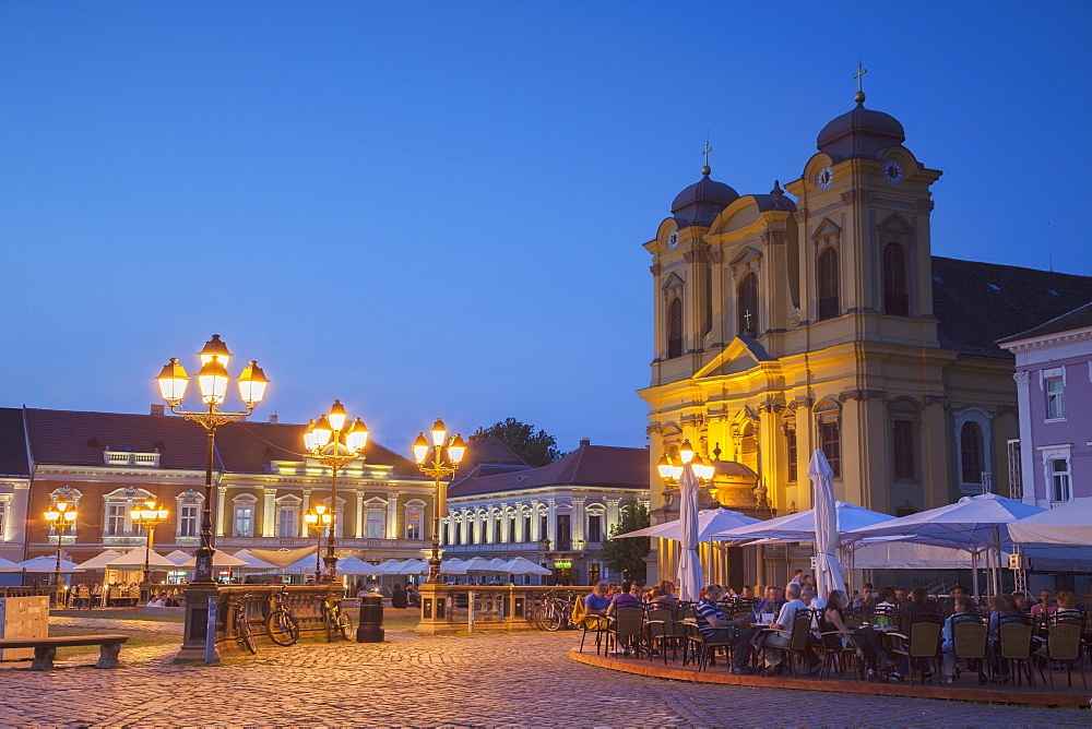 Roman Catholic Cathedral and outdoor cafes in Piata Unirii at dusk, Timisoara, Banat, Romania, Europe 