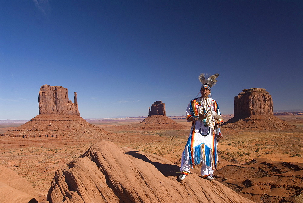 Navajo man in traditional costume, with Merrick Butte on the right, East Mitten in the center and West Mitten Butte on the left in the background, Monument Valley Navajo Tribal Park, Utah, United States of America, North America