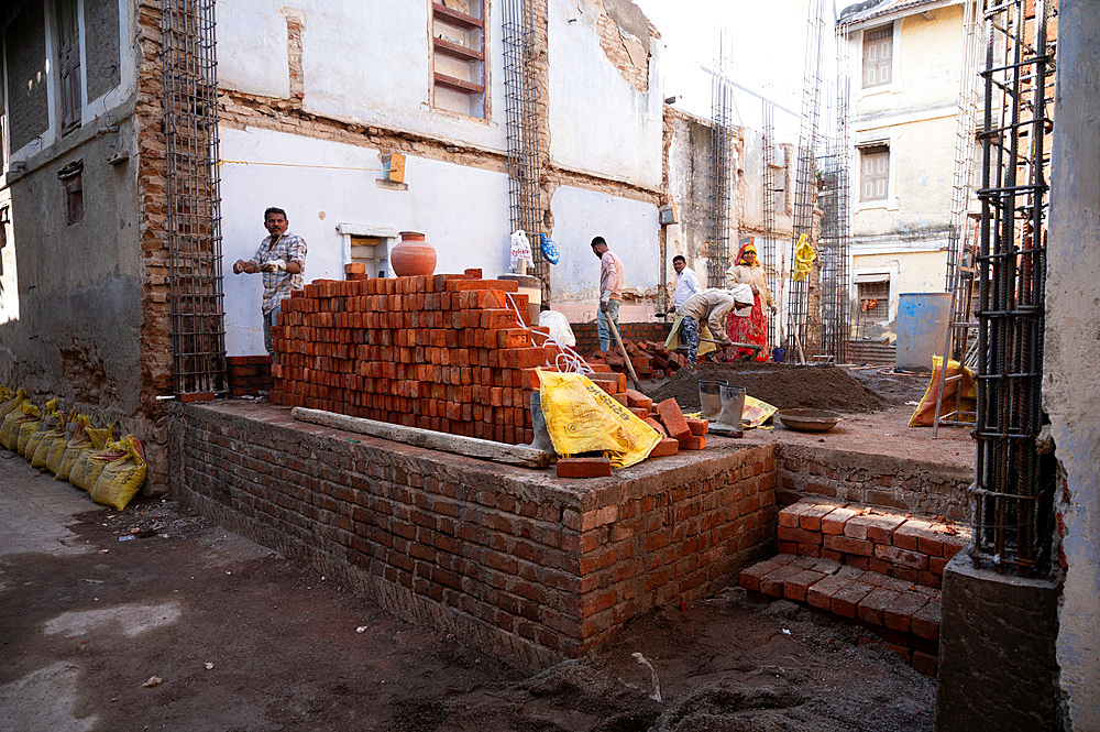 Both men and women working on a back street building site constructing a new house