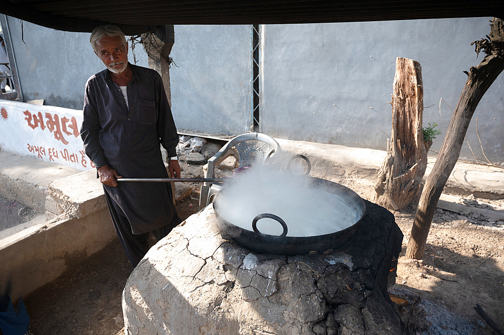 Street dahi (curd) maker stirring the dahi in a metal bowl over a clay covered oven