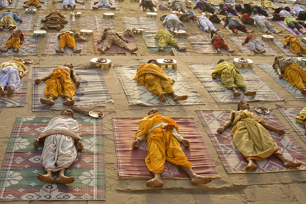 Students of a Sanskrit school performing the savasana (corpse) posture during daily yoga lesson at sunrise, on the ghat of Varanasi, Uttar Pradesh, India, Asia