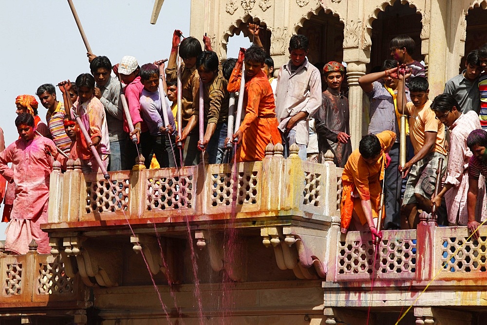 Young men celebrating Holi festival by splashing colored fluids on temple visitors, Nandgaon, Uttar Pradesh, India, Asia