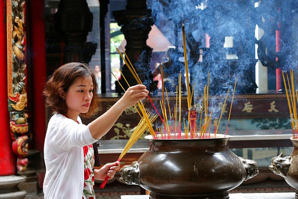 Buddhist worshipper placing incense sticks on joss stick pot, Taoist temple, Phuoc An Hoi Quan Pagoda, Ho Chi Minh City, Vietnam, Indochina, Southeast Asia, Asia