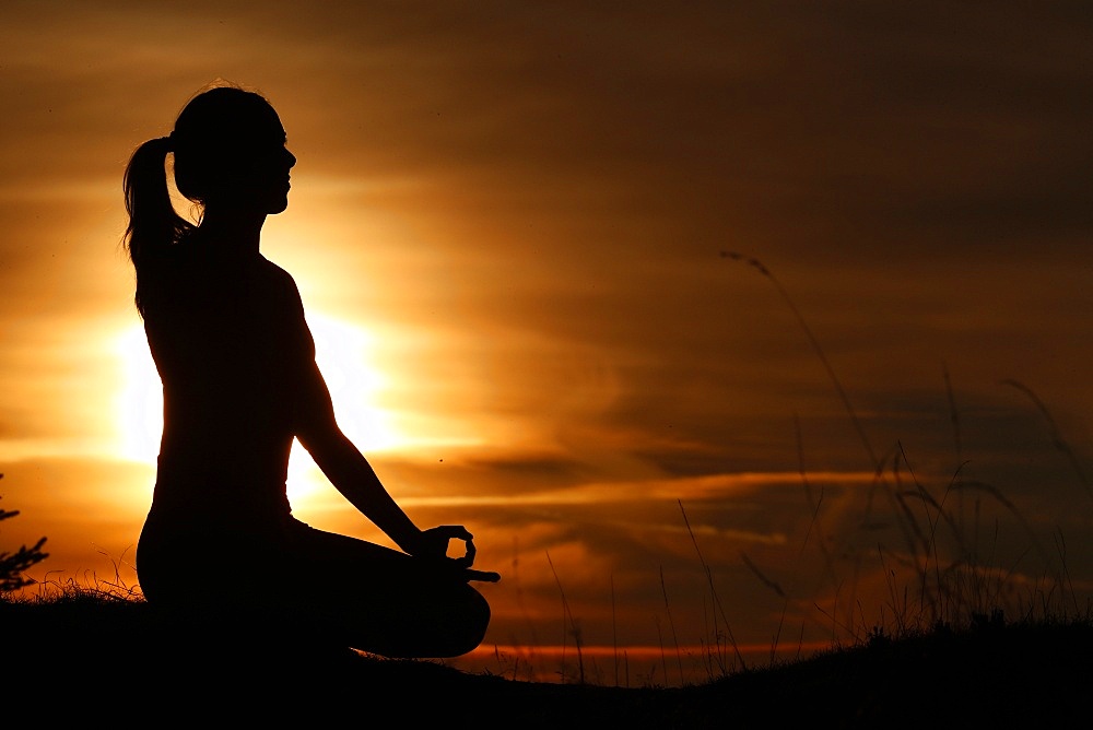 Silhouette of a woman in lotus position, practising yoga against the light of the evening sun, French Alps, France, Europe