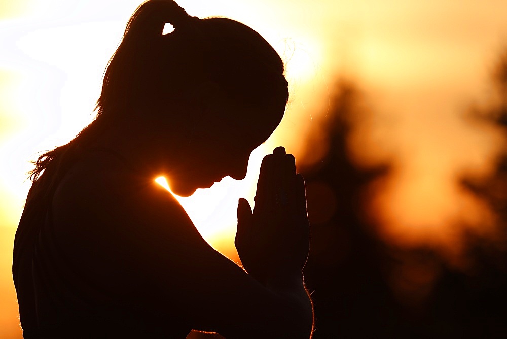 Silhouette of a woman practising yoga against the light of the evening sun, French Alps, France, Europe