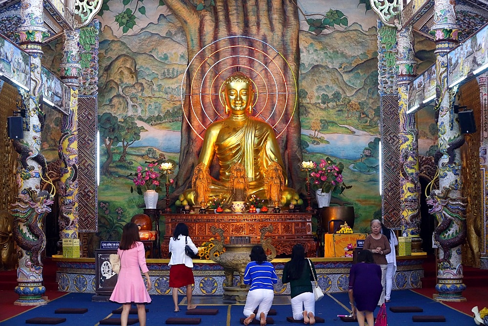 Sitting golden Buddha figure in main hall and worshippers praying to the Buddha, Linh Phuoc Pagoda, Dalat, Vietnam, Indochina, Southeast Asia, Asia