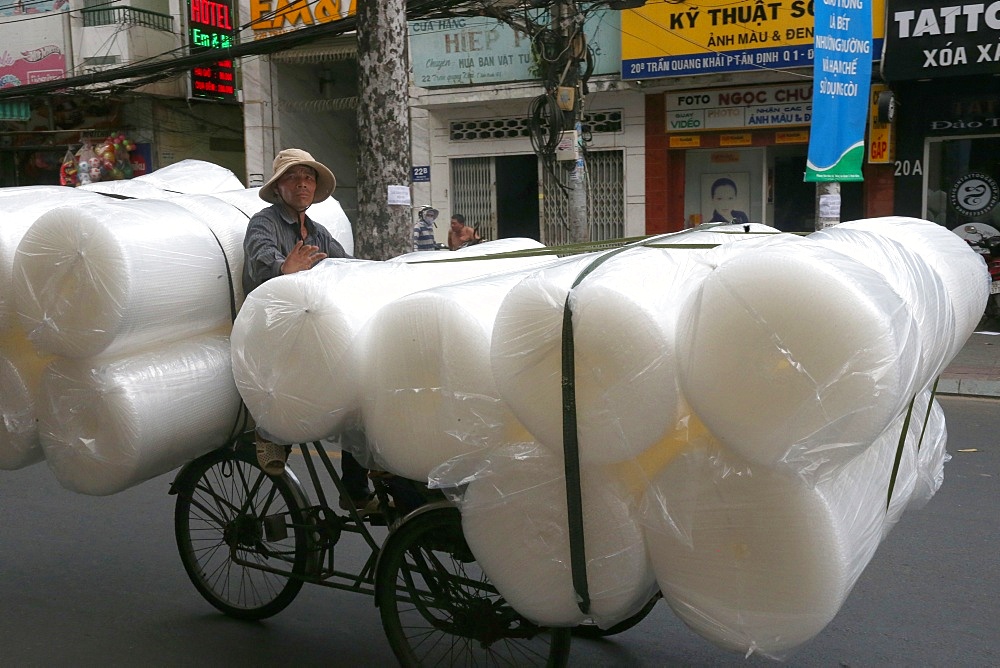 Man pedals a trishaw, loaded with rolls on a road, Ho Chi Minh City, Vietnam, Indochina, Southeast Asia, Asia