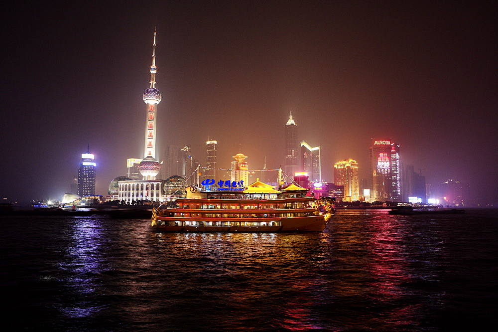 Boat set against Shanghai illuminated skyline, Shanghai, China, Asia