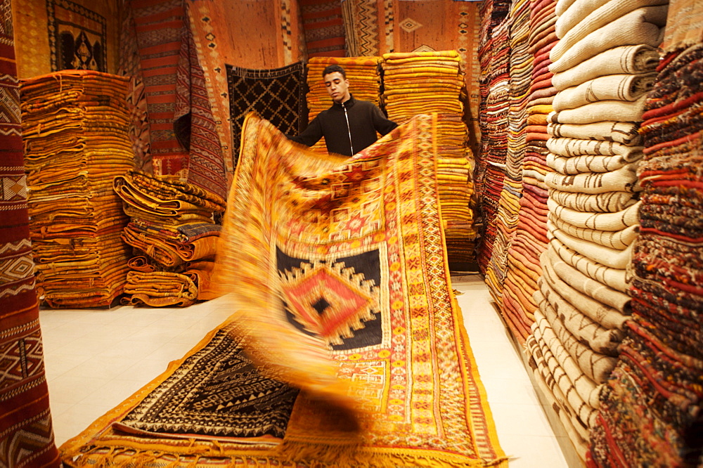 Carpet shop interior with shop keeper showing rug, Marrakesh, Morocco, North Africa, Africa