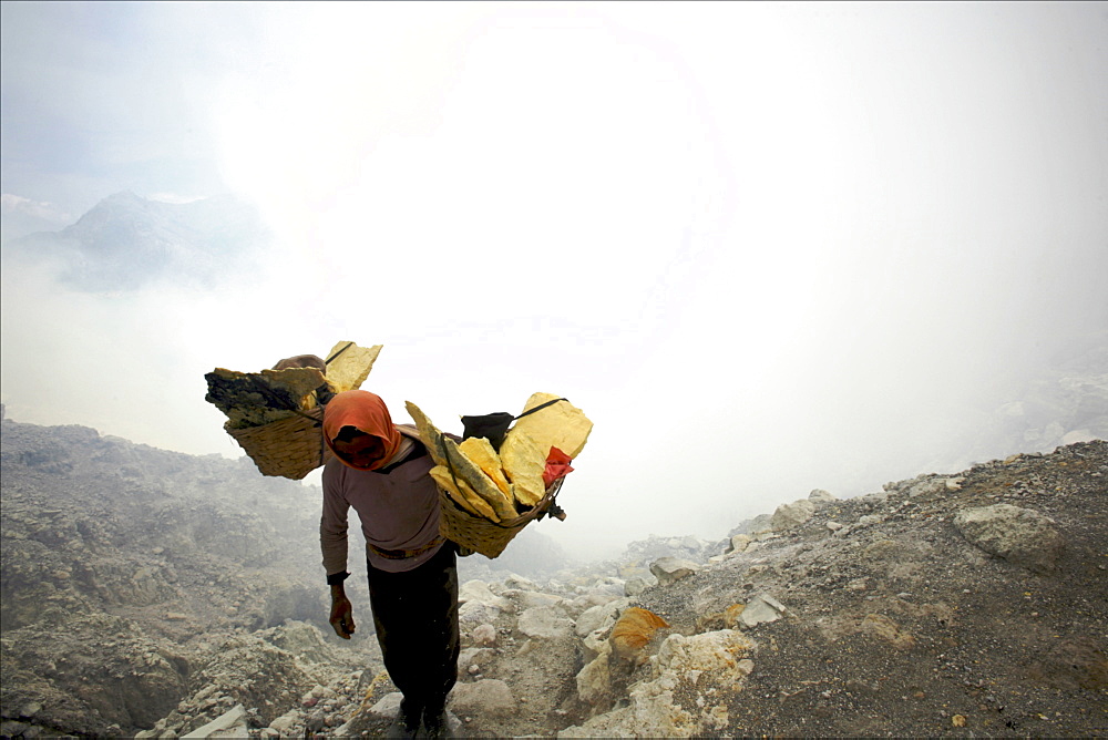 Worker carrying heavy baskets of sulphur, by the crater lake of the Kawa Ijan volcano where a sulphur mine constantly smokes, Baluran National Park, Java, Indonesia, Southeast Asia, Asia