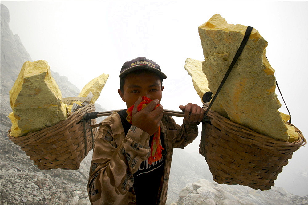 Worker carrying heavy baskets of sulphur, by the crater lake of the Kawa Ijan volcano, where a sulphur mine constantly smokes, Baluran National Park, Java, Indonesia, Southeast Asia, Asia