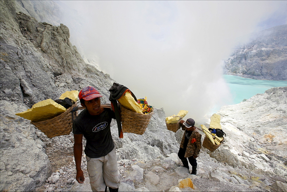 Workers carrying heavy baskets of sulphur, by the crater lake of the Kawa Ijan volcano where a sulphur mine constantly smokes, Baluran National Park, Java, Indonesia, Southeast Asia, Asia