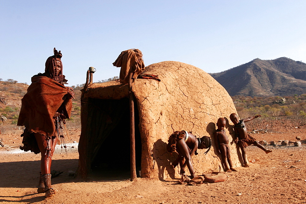 A Himba woman and children outside her house in a village on the Kunene River, on the border with Angola, Namibia, Africa