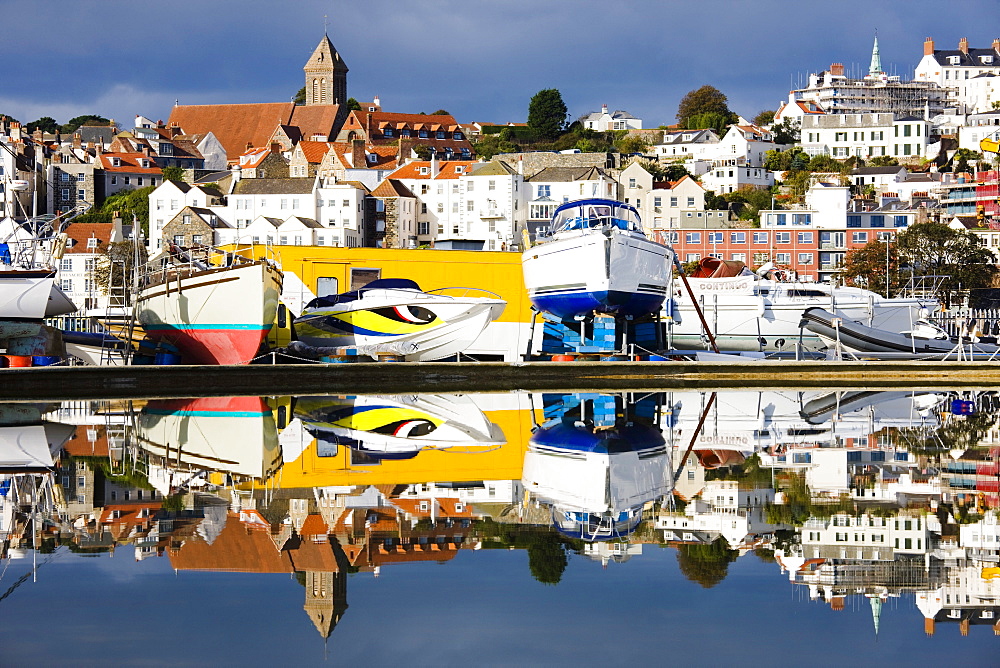 St. Peter Port and harbour side boats stored on dry dock reflected in a model boat pond in Guernsey, Channel Islands, United Kingdom, Europe