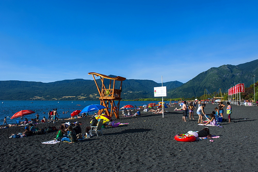 Tourists sunbathing on the volcanic sand beach on Lago Villarrica, Pucon, Chile, South America 