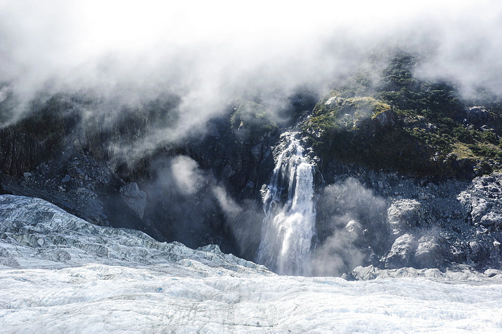 Aerial of a waterfall flowing into the icefield of Fox Glacier, Westland Tai Poutini National Park, South Island, New Zealand, Pacific