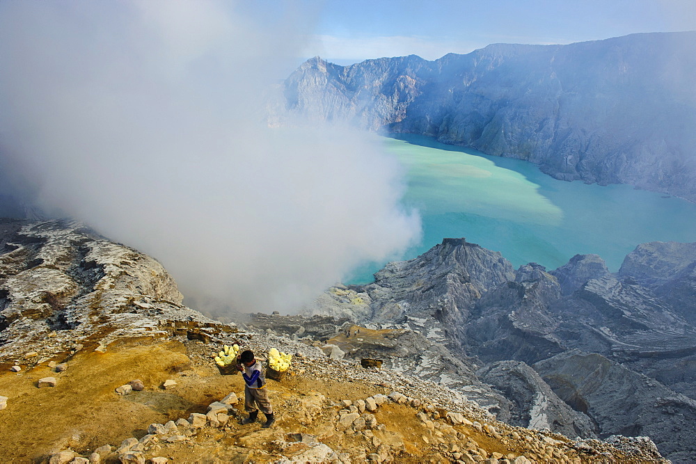 Worker loaded with big pieces of sulphur in front of steam clouds on the Ijen crater lake, Java, Indonesia, Southeast Asia, Asia