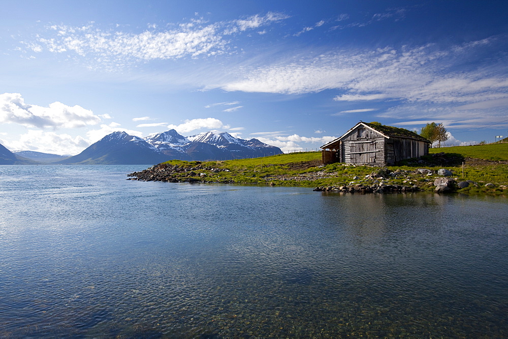 Cabin with traditional grass roof overlooking a fjord and snowy mountains in Lyngen Peninsula, Troms county, Norway, Scandinavia, Europe