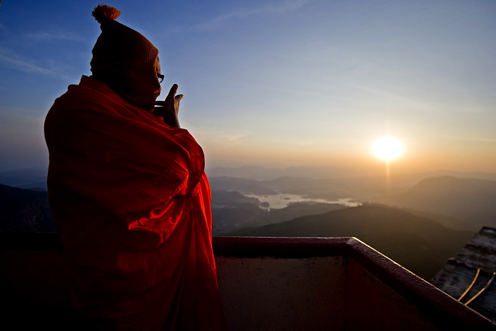 A monk looks out over a sunrise from the top of the sacred mountain Sri Pada (Adam's Peak), Sri Lanka, Asia 