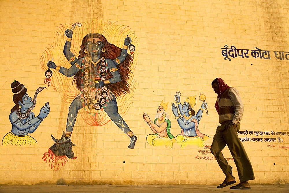 An Indian man walks by a wall painted with images of Hindu deities in Varanasi, Uttar Pradesh, India, Asia