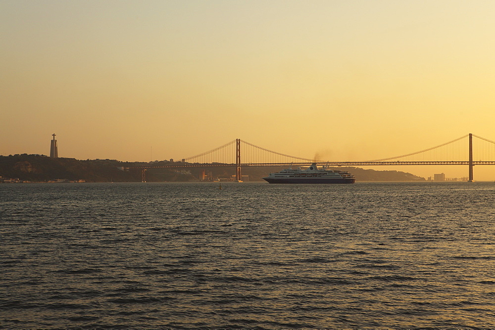 A cruise liner turns into the sunset, on the River Tagus under the 25 April Bridge and Christus Rei statue, Lisbon, Portugal, Europe