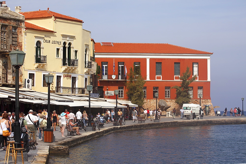 People walk by the waterfront restaurants and cafes within the Venetian harbour at Chania (Canea), Crete, Greek Islands, Greece, Europe