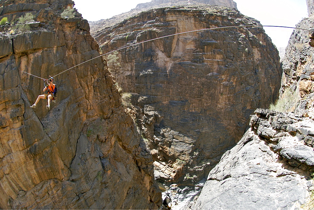 A hiker traversing a zip-wire (aka flying fox) on the Via Ferrata hike in Snake Canyon, part of Wadi Bani Auf in Jebel Akhdar of the western Hajar mountains in Oman.