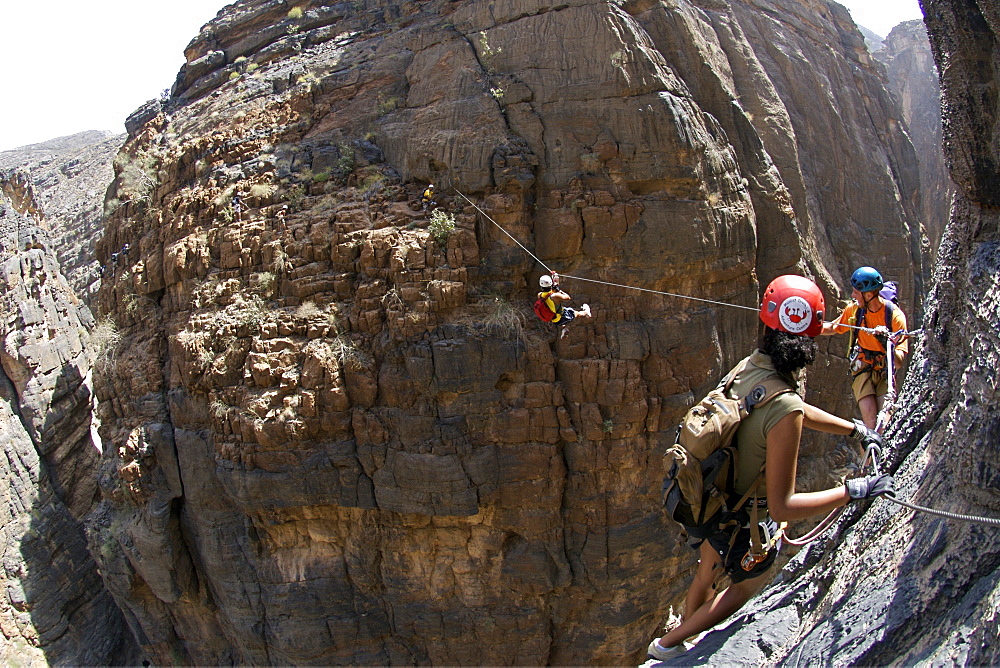 A hiker traversing a zip-wire (aka flying fox) on the Via Ferrata hike in Snake Canyon, part of Wadi Bani Auf in Jebel Akhdar of the western Hajar mountains in Oman.