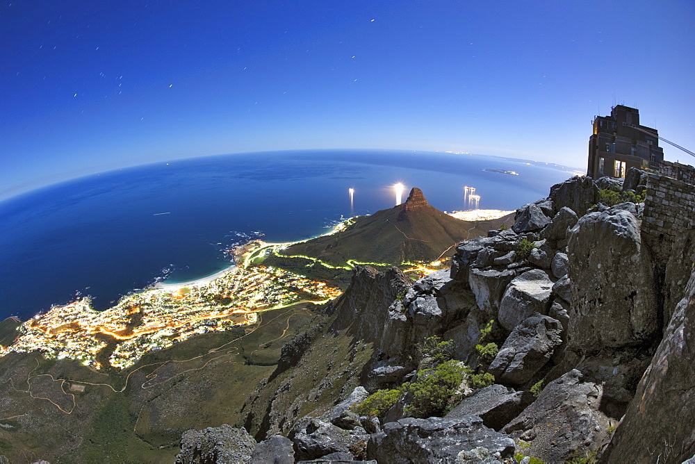 Night-time, moonlit view of the Table Mountain upper cable car station, Camps bay, the Atantic Ocean and Lion's Head in Cape Town, South Africa.