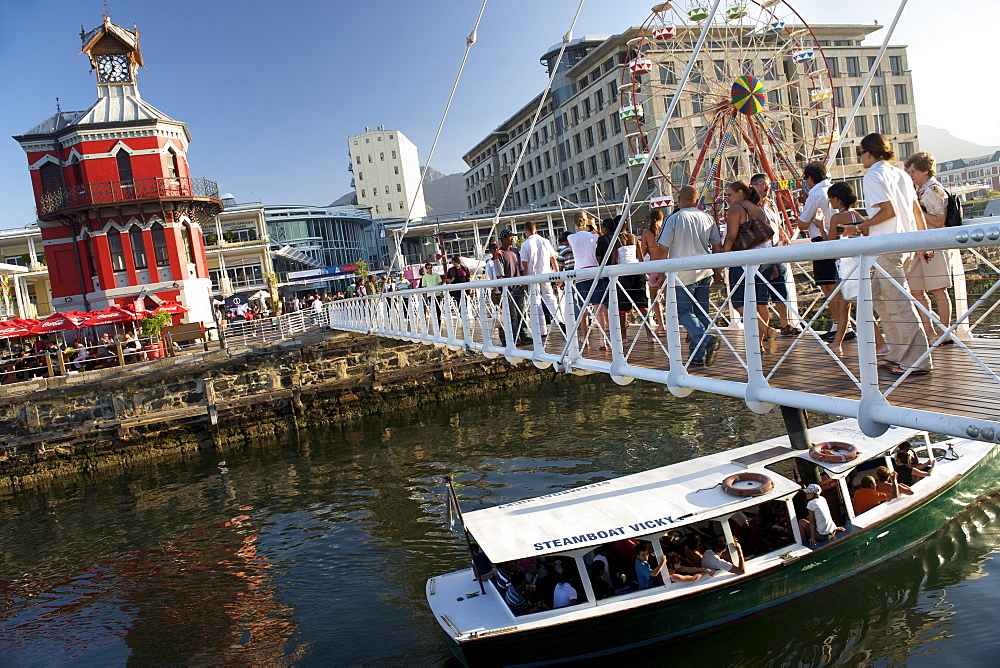 Small boat passing under the pedestrian bridge at the clock tower in Cape Town's Victoria & Alfred waterfront.