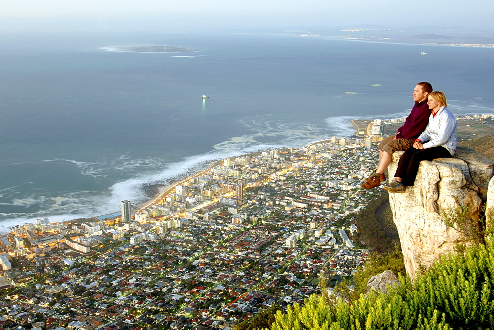 A couple observe the dusk view of Robben Island and Cape Town's Atlantic seaboard from the summit of Lion's Head.