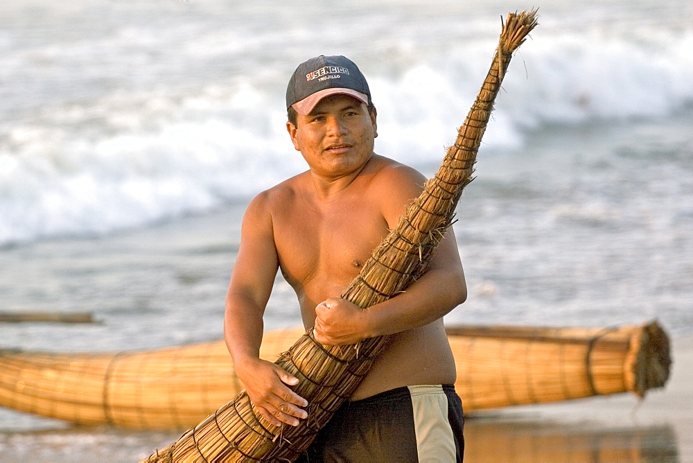 Fisherman with 'caballito (little horse) de totora' reed boat on the beach at the popular far north coast fishing & surfing village of Huanchaco, near Trujillo, Peru, South America.