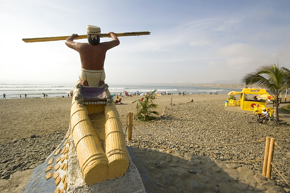 Statue of fisherman with 'caballito (little horse) de totora' reed boat on the beach at the popular far north coast fishing & surfing village of Huanchaco, near Trujillo, Peru, South America