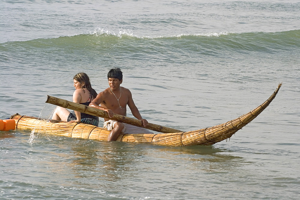 Tourist girl on a 'caballito (little horse) de totora' reed boat at the popular far north coast fishing & surfing village of Huanchaco, near Trujillo, Peru, South America.