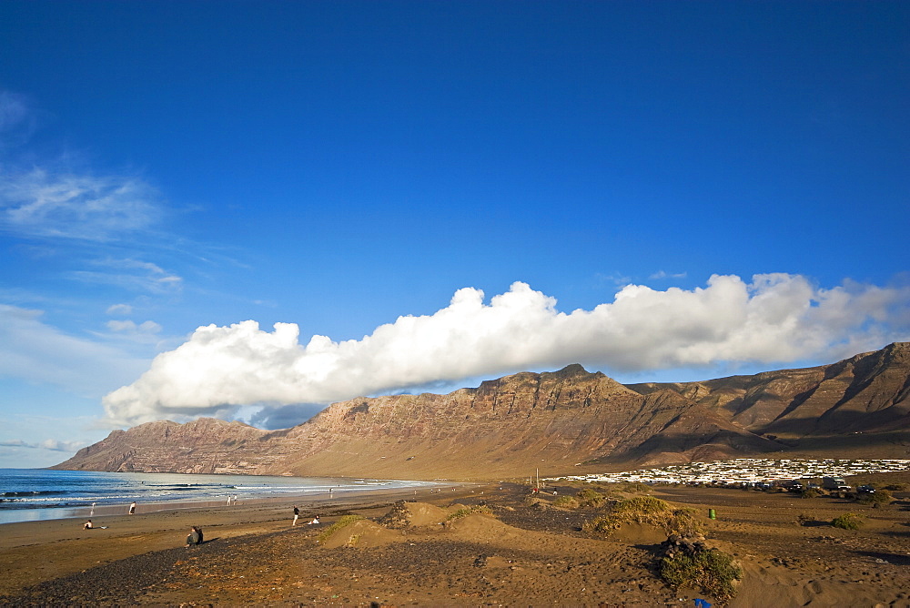 Spectacular 600m volcanic cliffs of the Risco de Famara rising over Lanzarote's finest beach at Famara, with its low-rise bungalow development, Famara, Lanzarote, Canary Islands, Spain, Atlantic Ocean, Europe