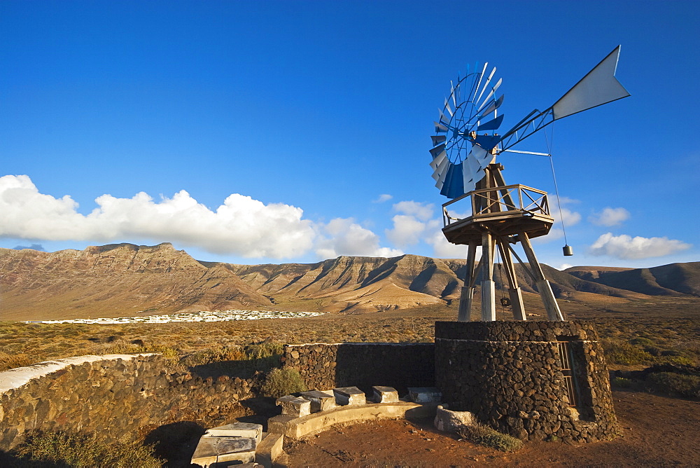 Traditional wind pump with 600m volcanic cliffs of the Risco de Famara rising over desert landscape near Famara in the north west of the island, Famara, Lanzarote, Canary Islands, Spain, Atlantic Ocean, Europe