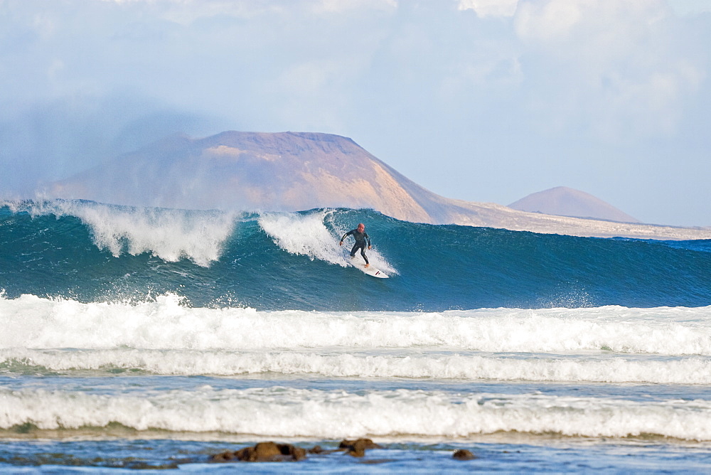 Surfer on a large wave with Graciosa Island beyond, at the world class surf reef break known as San Juan, east of Famara in the north of the island, Famara, Lanzarote, Canary Islands, Spain, Atlantic, Europe