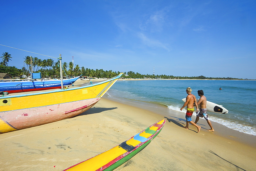 Surfers and fishing boats on this popular surf beach, badly hit by the 2004 tsunami, Arugam Bay, Eastern Province, Sri Lanka, Asia