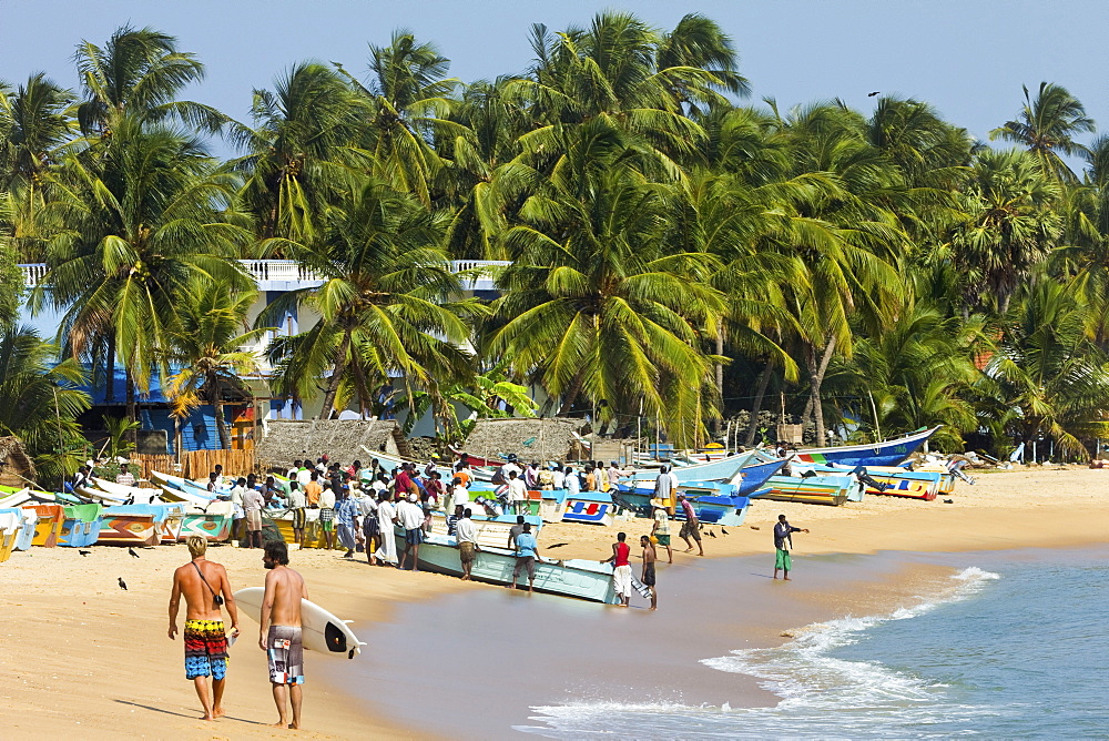 Tourists stroll whilst local fishermen work on this popular surf beach, Arugam Bay, Eastern Province, Sri Lanka, Asia