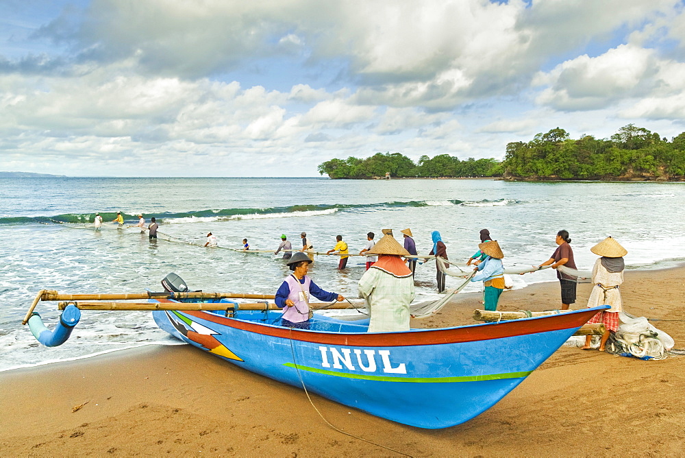 Outrigger fishing boat and people pulling net in by hand to shore near Batu Karas, Pangandaran, West Java, Java, Indonesia, Southeast Asia, Asia