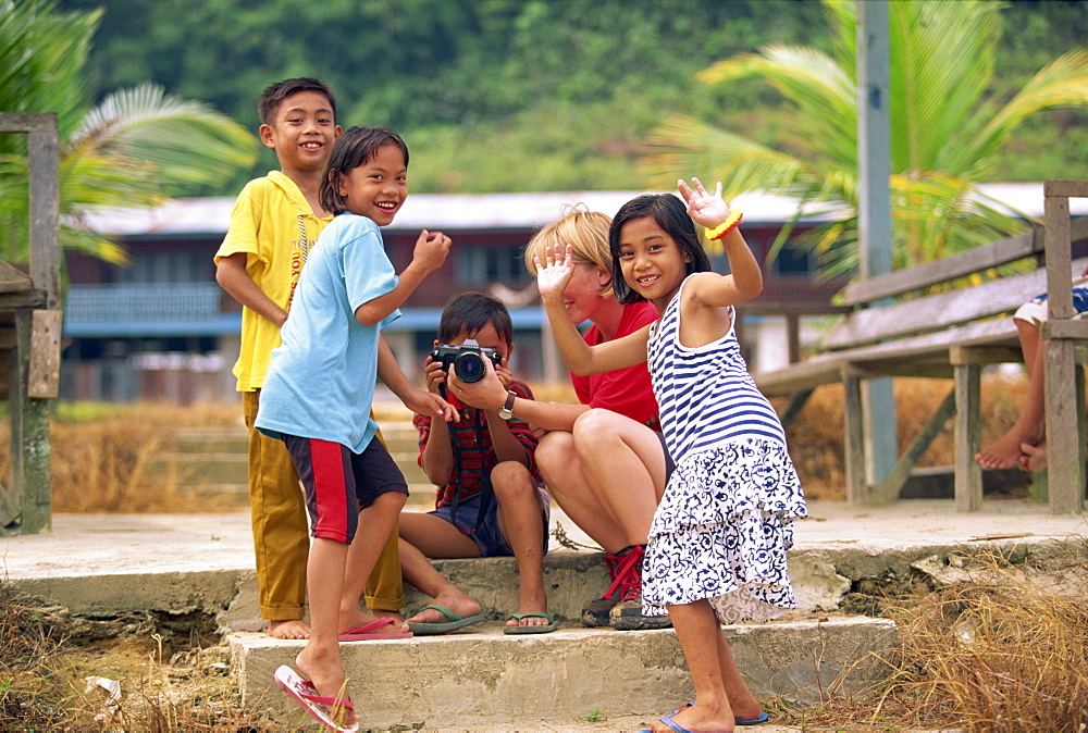 A group of Iban Dayak children with a tourist and camera outside their longhouse on the Rajang River near Kapit in Sarawak, northwest Borneo, Malaysia, Southeast Asia, Asia