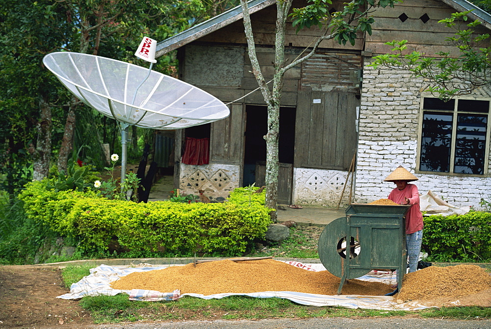 Satellite dish and man with rice winnowing machine, Lake Maninjau, Sumatra, Indonesia, Southeast Asia, Asia