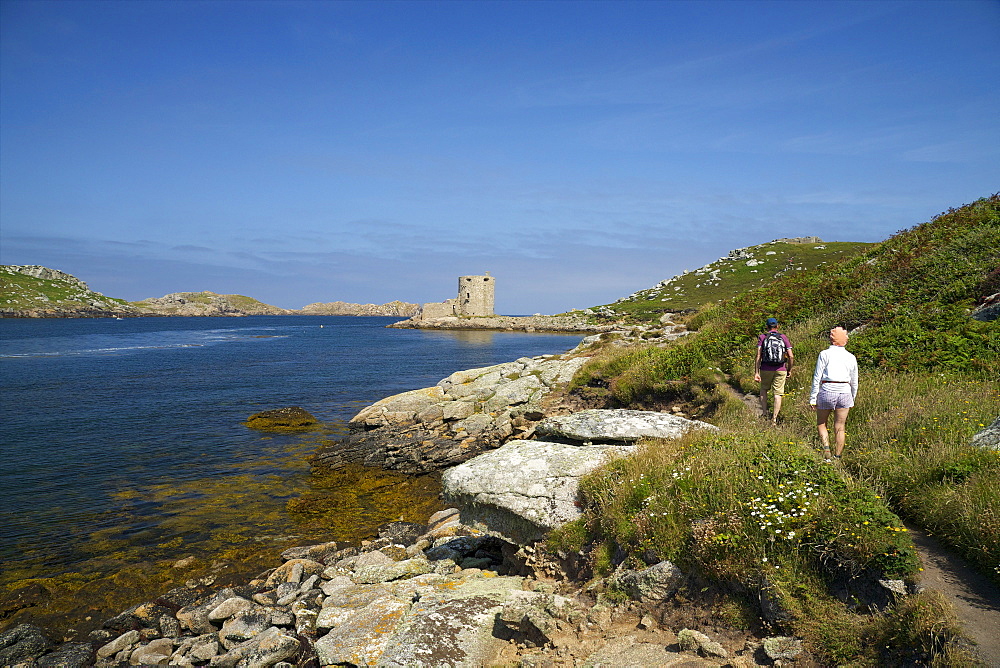 Walkers near Cromwell's Castle in summer sunshine, Isle of Tresco, Isles of Scilly, United Kingdom, Europe 