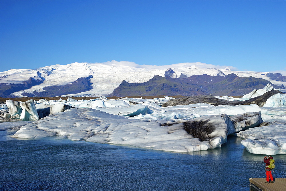 Man taking photo of icebergs on the glacial lake at Jokulsarlon with snow on the massive icecap of Vatnajokull behind, Iceland, Polar Regions