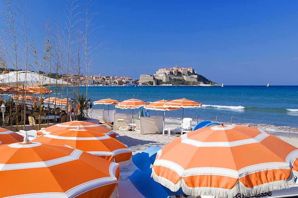 Sun umbrellas on beach, view of the citadel of Calvi, Balagne, Corsica, France, Europe