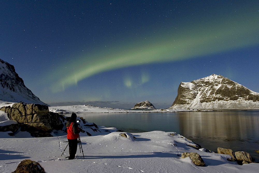 Photographer taking pictures of Polar lights (Aurora borealis), in the Vikbukta bay, Vestvagoya, Lofoten, Norway, Europe