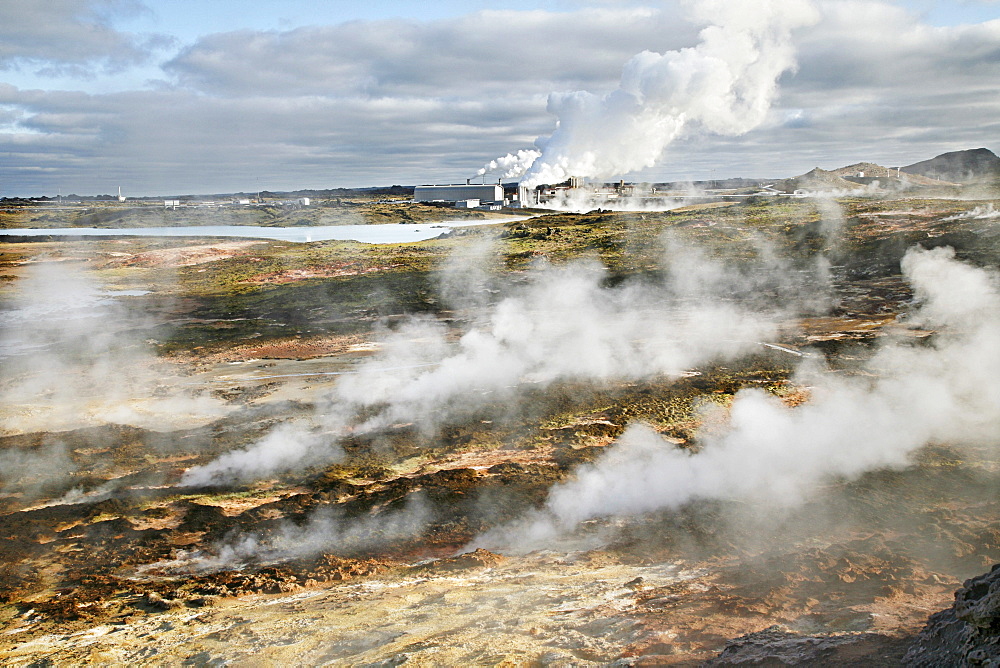 Steam from the countless holes and fractures in the earth's crust, the Solfatarten, behind it a geothermal power station and a factory for salt extraction, which is operated with geothermal energy, geothermal region of Gunnuhver, southern Iceland, Iceland