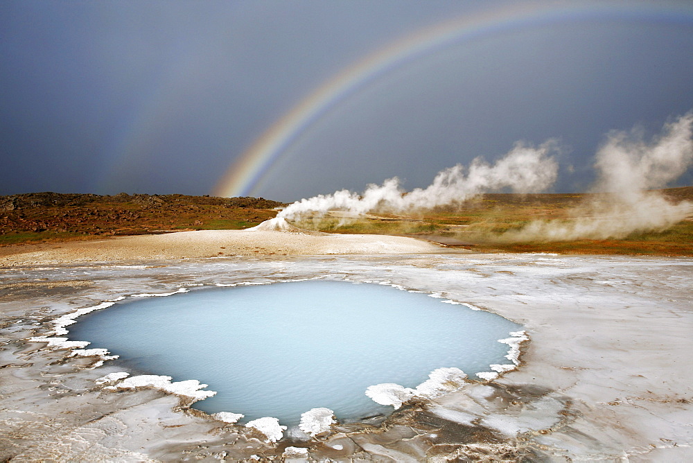 Blahver, blue spring, the most beautiful blue water pool in Hveravellir in the Highlands, in front of Oeskjuholt, a steaming calc-sinter mound which looks like a mini volcano, below a rainbow, Hveravellir, Iceland, Europe