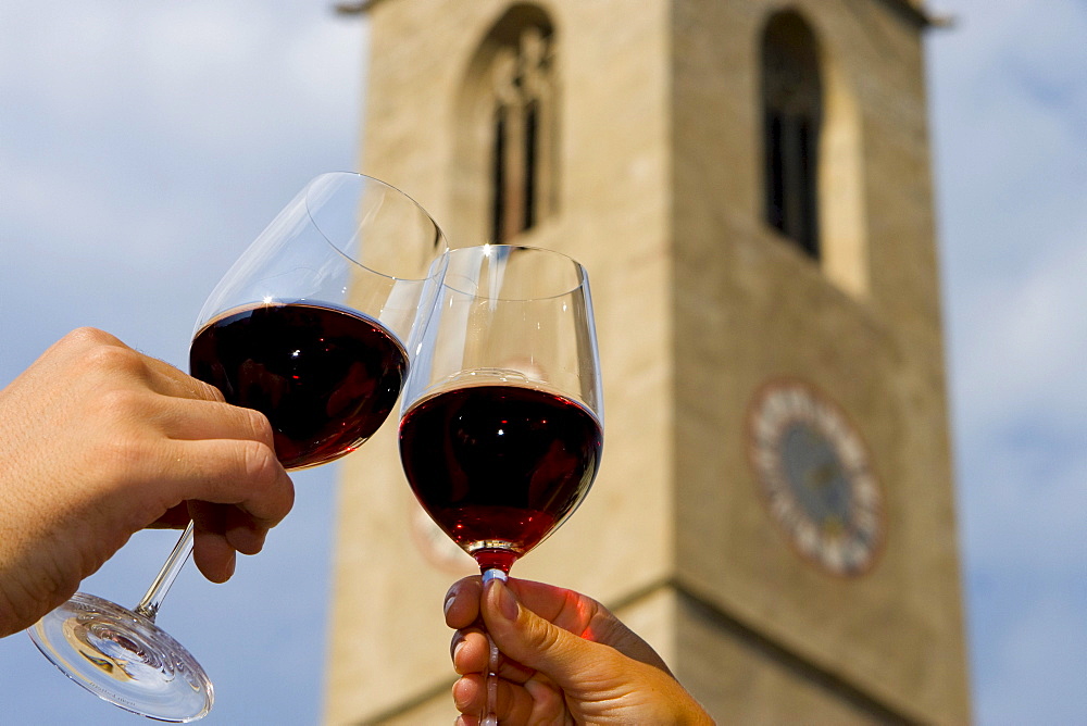 Red wine glasses clinking, steeple in Kaltern, South Tyrol, Italy, Europe