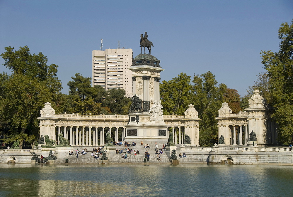 View over an artificial lake towards people in front of a monument with an equestrian statue of King Alfosno XII, Parque del Buen Retiro, Park of the Pleasant Retreat or El Retiro, Madrid, Spain, Europe